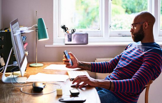 Individual working on his phone and computer, representing a better user experience with Modern Workspaces.